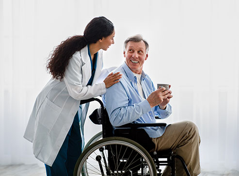 Female doctor talking to senior male patient who is sitting in a wheelchair and holding a cup
