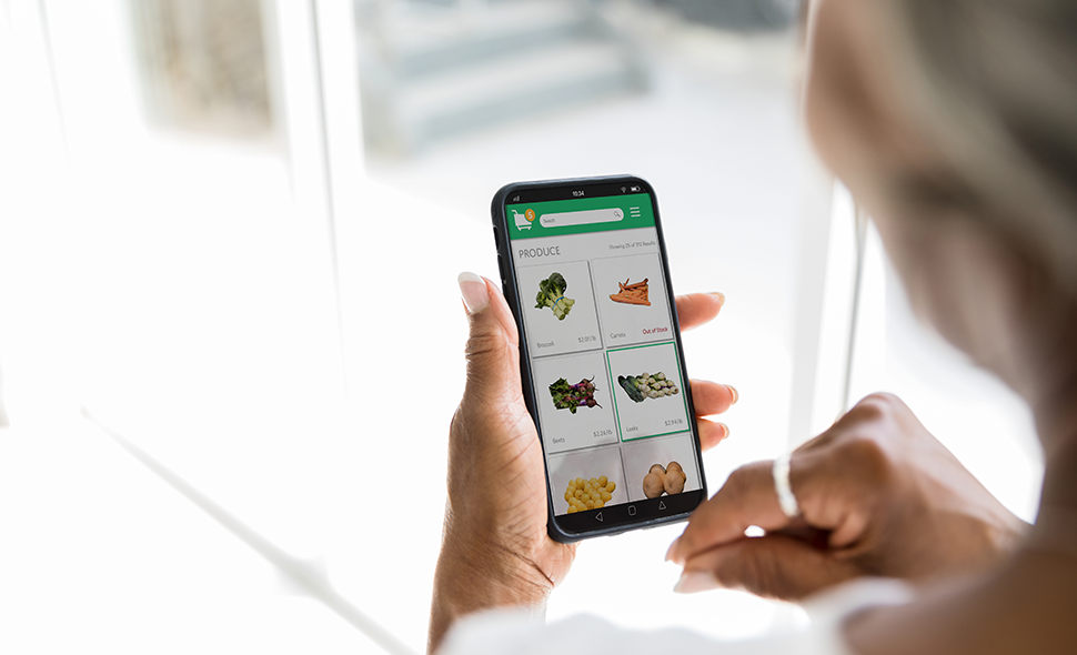 Person holding a phone showing an online grocery shopping cart.