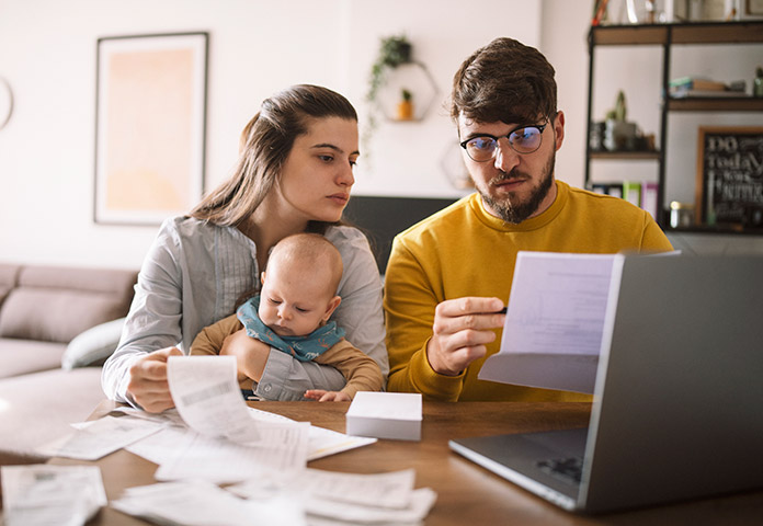 Couple holding a baby while reviewing bills and a laptop, illustrating financial vulnerability