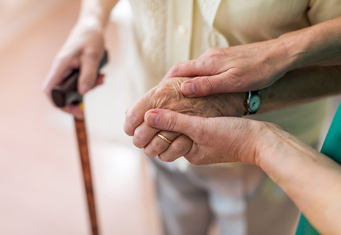 Senior’s hand holding a cane, held by another hand, illustrating frailty and care