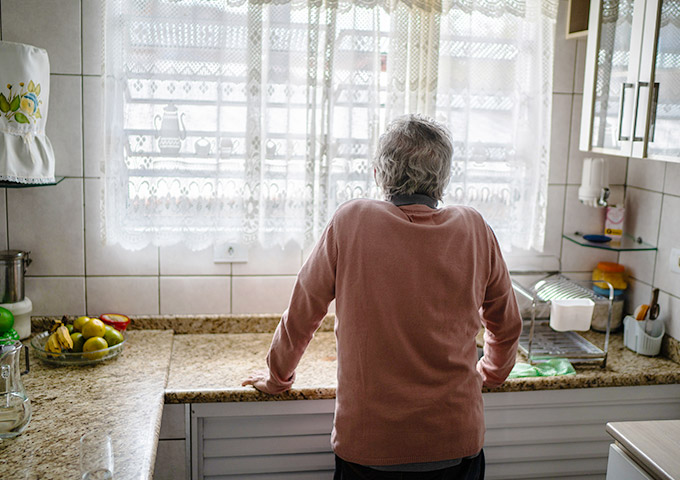 Person standing at a kitchen sink looking out a window, illustrating social vulnerability
