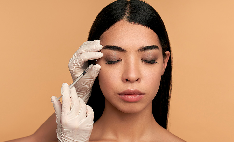 Person receiving a cosmetic injection near the eyebrow from a gloved practitioner