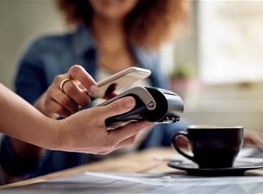 Person paying by phone at a card terminal beside a coffee cup, illustrating channel strategy analytics