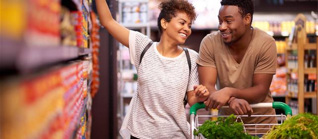 Smiling couple shopping for groceries together in a supermarket aisle, representing the consumer packaged goods category