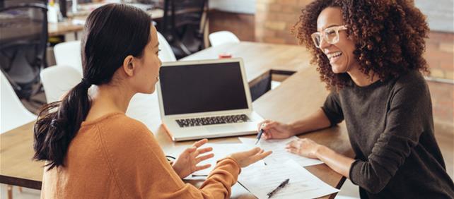 Two women seated at a table talking over a laptop, representing the credit union industry category