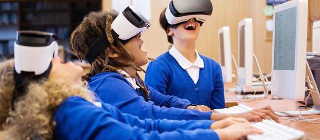 Students in uniforms wearing virtual reality headsets while working at computers in a classroom