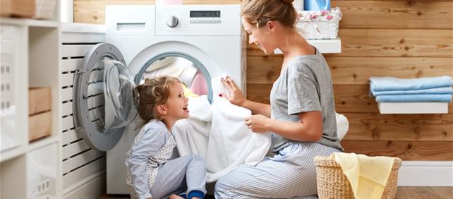 Parent and child laughing while loading a front-loading washing machine, illustrating household energy use