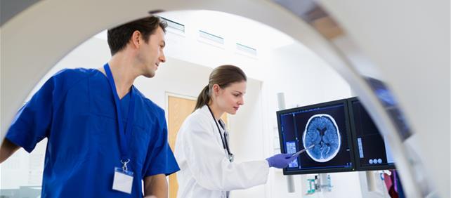 Two healthcare workers reviewing a medical scan on a monitor beside a scanner