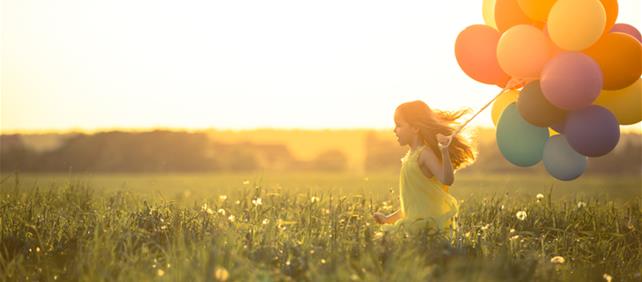 Child holding colourful balloons in a sunlit field, illustrating the insurance industry
