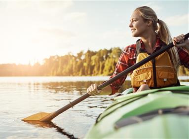 Person kayaking on a calm lake at sunset, surrounded by nature