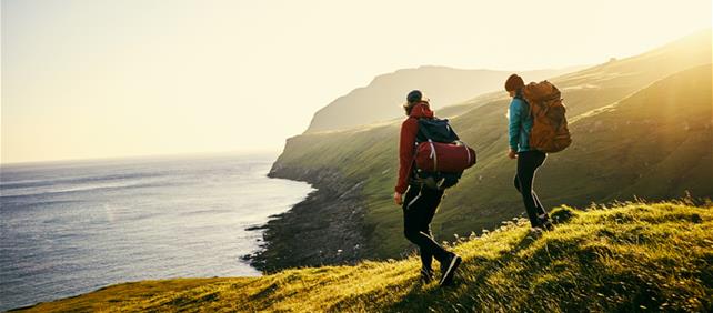 Two hikers walking along a coastal headland at sunset, representing travel and leisure