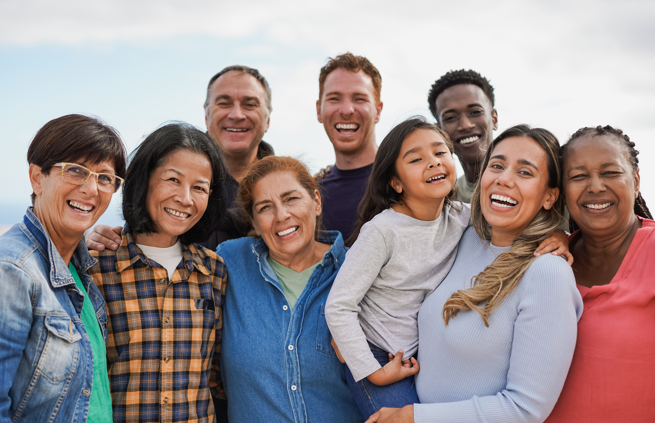 Group of multigenerational people hugging each other while smiling on camera