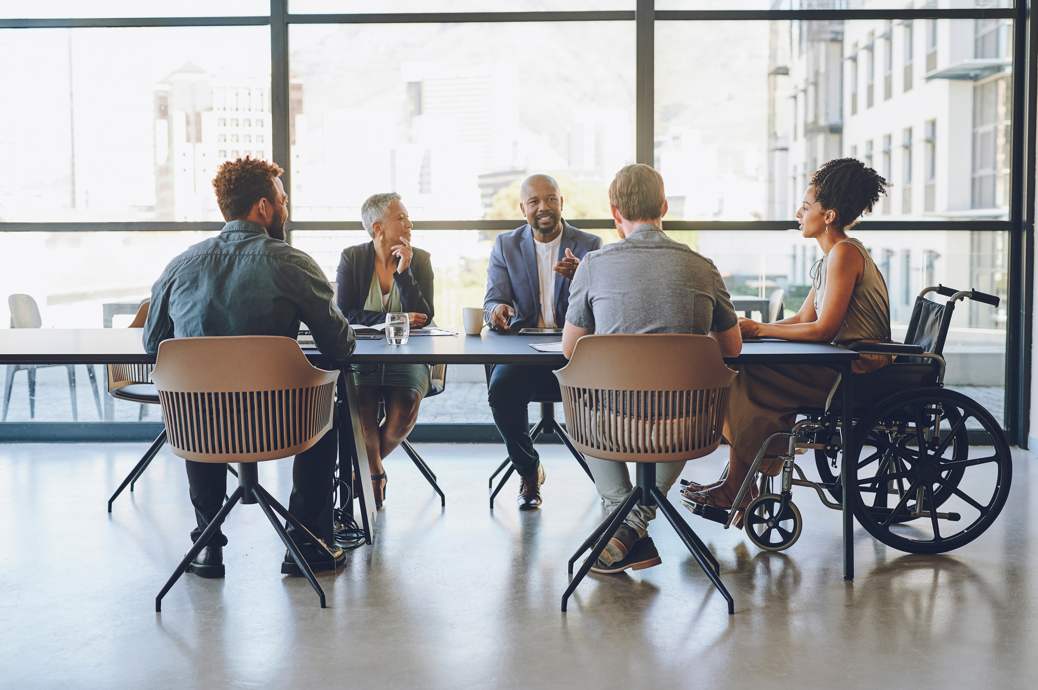 Five colleagues, including one in a wheelchair, meeting around a table in a bright office