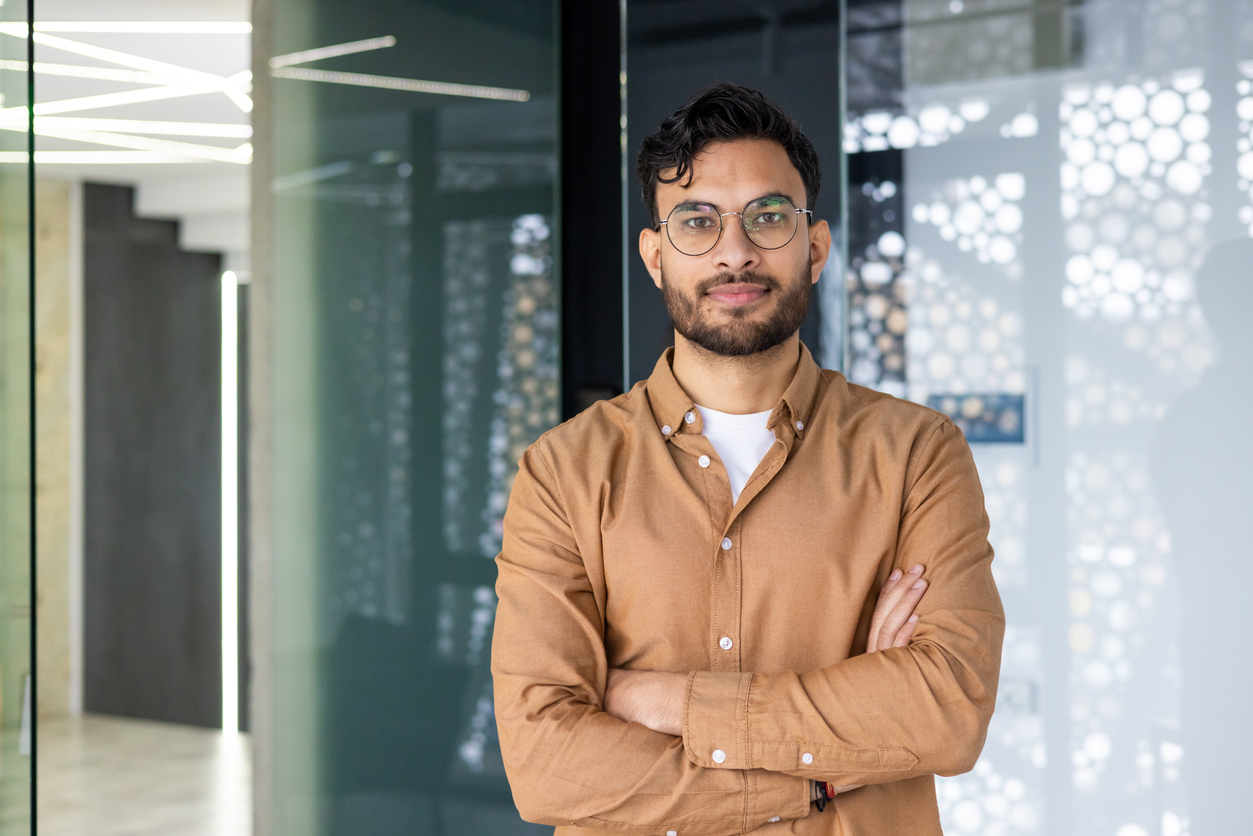 Confident young man with glasses standing and smiling in a modern office