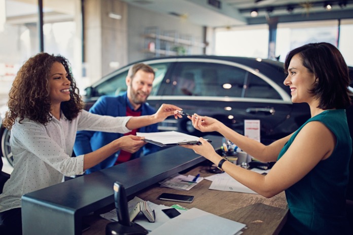 Couple receiving keys from a car salesperson while signing a contract at a dealership