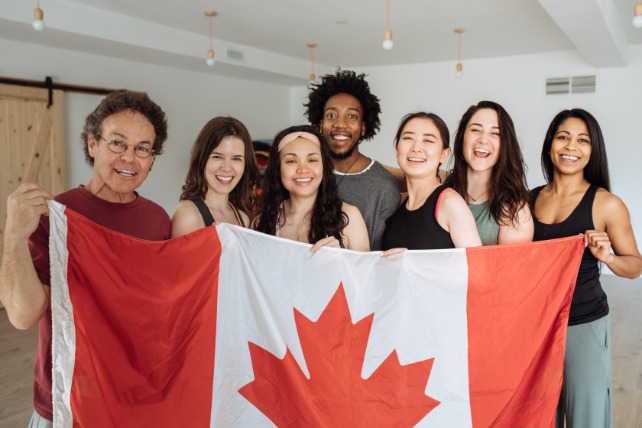 Group of people from different nationalities smiling and holding a Canadian flag together