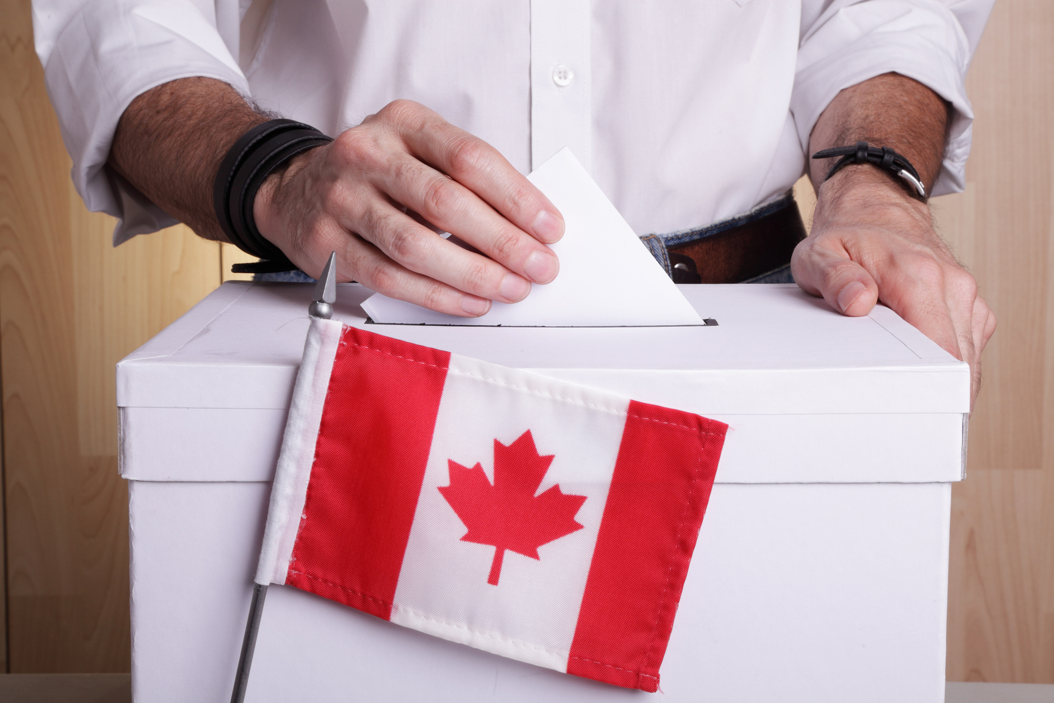 Person placing a voting ballot into a ballot box with a small Canadian flag in front
