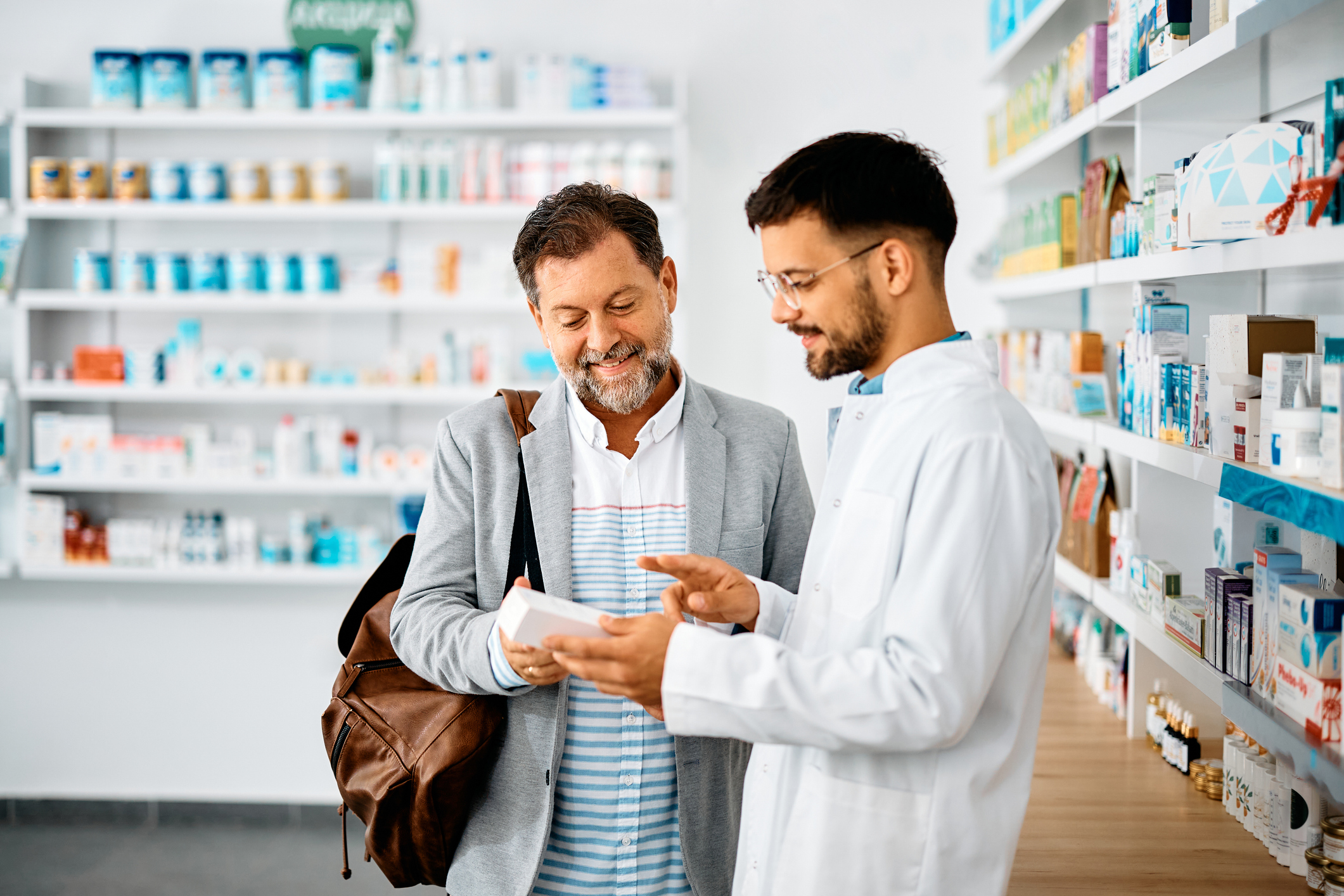 man choosing medicine with help of young pharmacist in drugstore