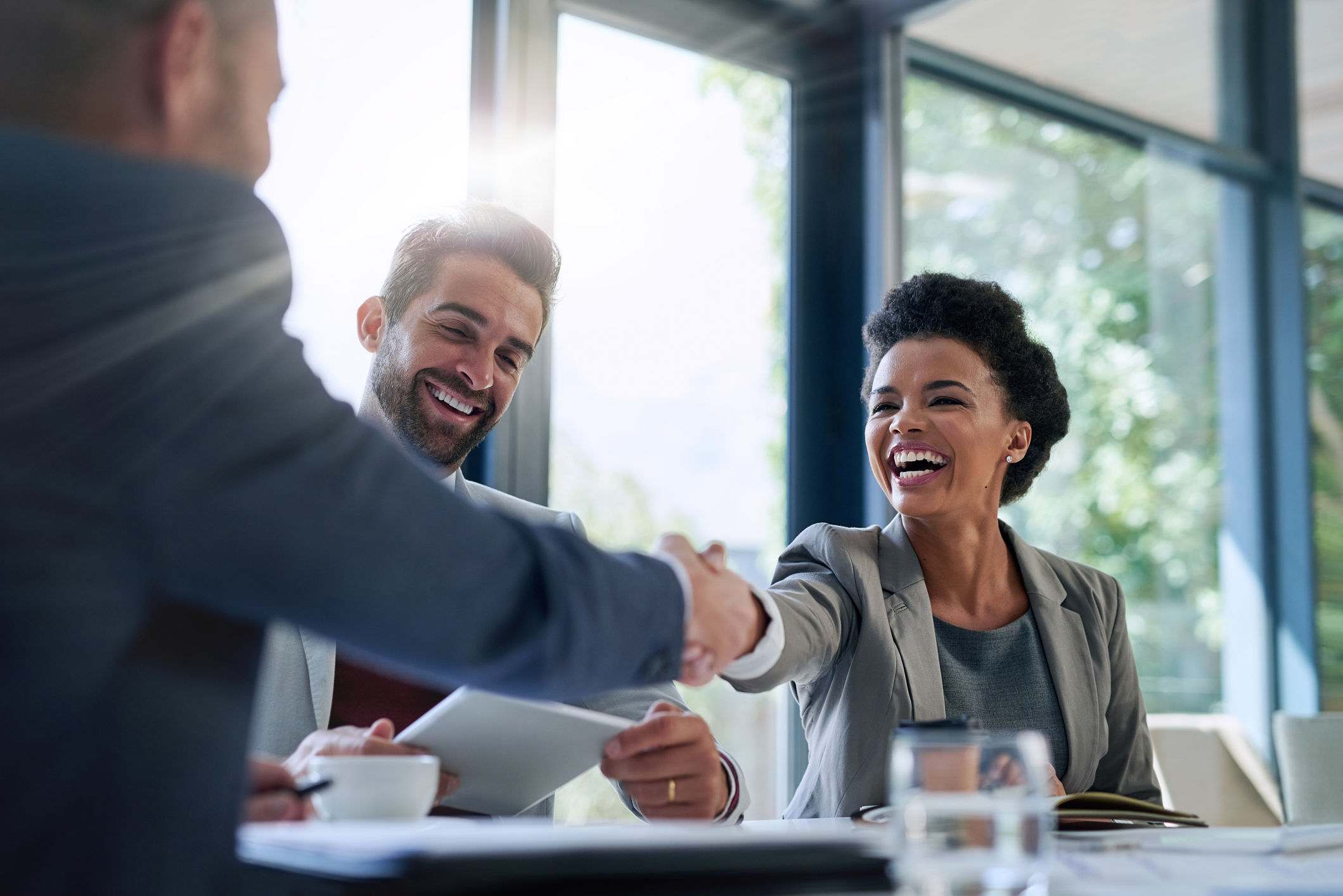 Three people sitting at a table with two of them shaking hands an smiling