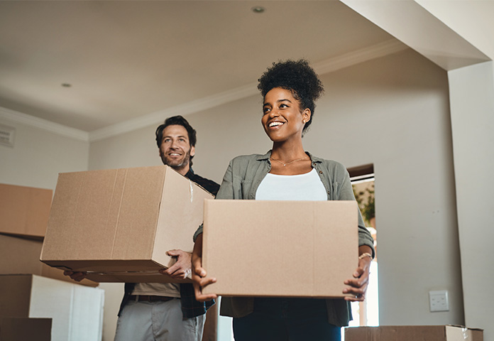 Biracial couple holding boxes and smiling while moving into a house